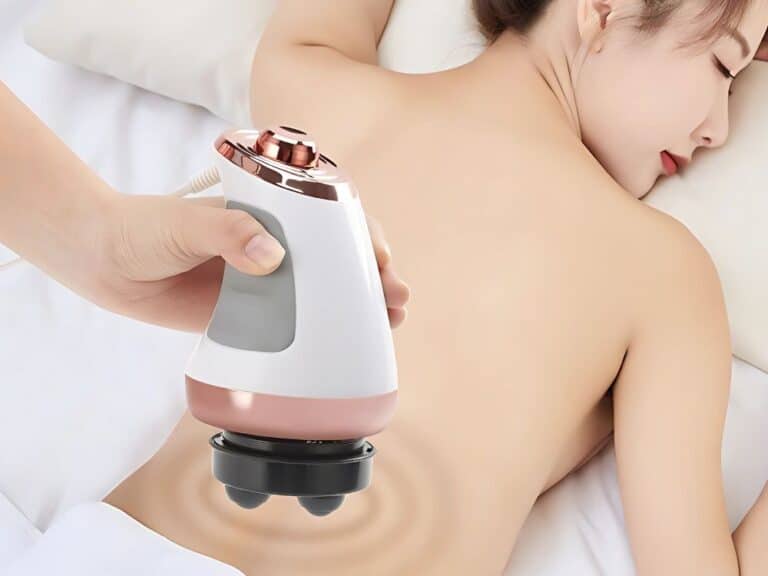 Masážní přístroj s ergonomickým designem bílo-růžové barvy, který je přiložen na záda odpočívající osoby na bílém lůžku.