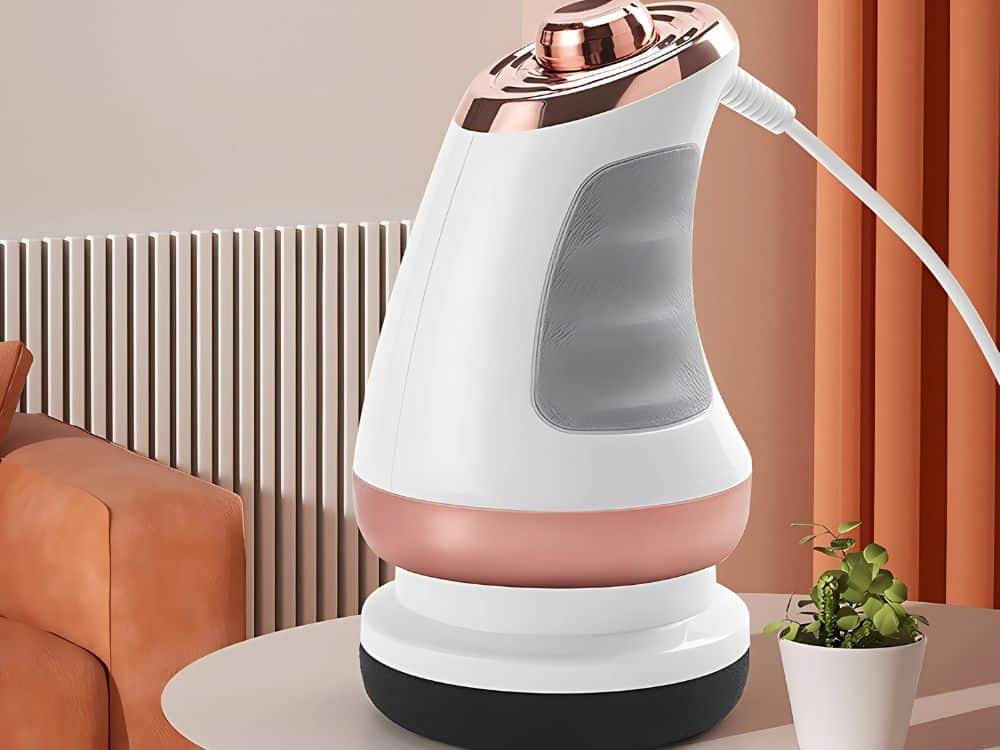 Moderní bezdrátová žehlička v bílé, měděné a šedé barvě s elegantním designem, umístěná na stole vedle hrnku s rostlinou a čalouněného křesla.