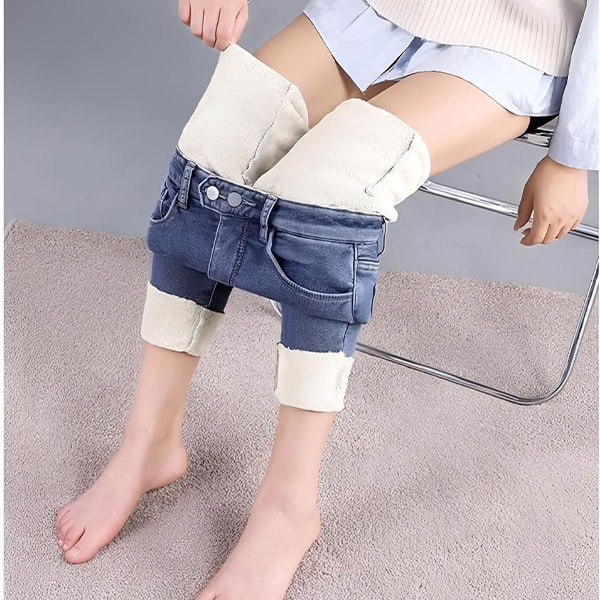 Modré džínové kraťasy s bílými lemovanými okraji, které jsou oblečené na nohou odpočívajícího člověka sedícího na šedém koberci.