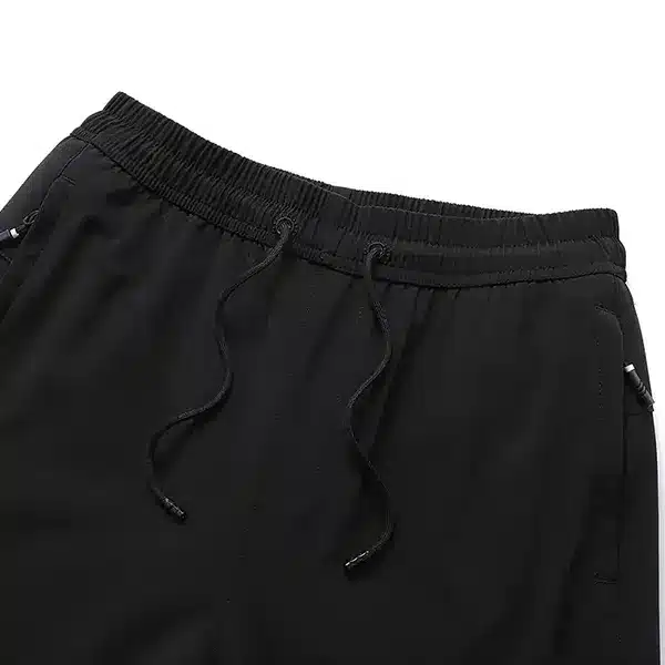 Černé sportovní kalhoty se stahovací šňůrkou v pase, detail na horní část kalhot se zipovou kapsou a elastickým pasem.