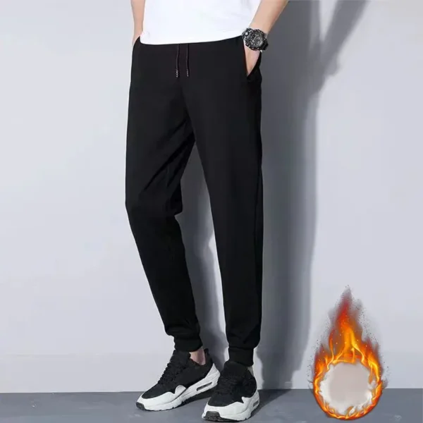 Černé pánské tepláky se zúženým střihem, vhodné pro volný čas, spolu s černobílými sportovními botami na neutrálním pozadí.