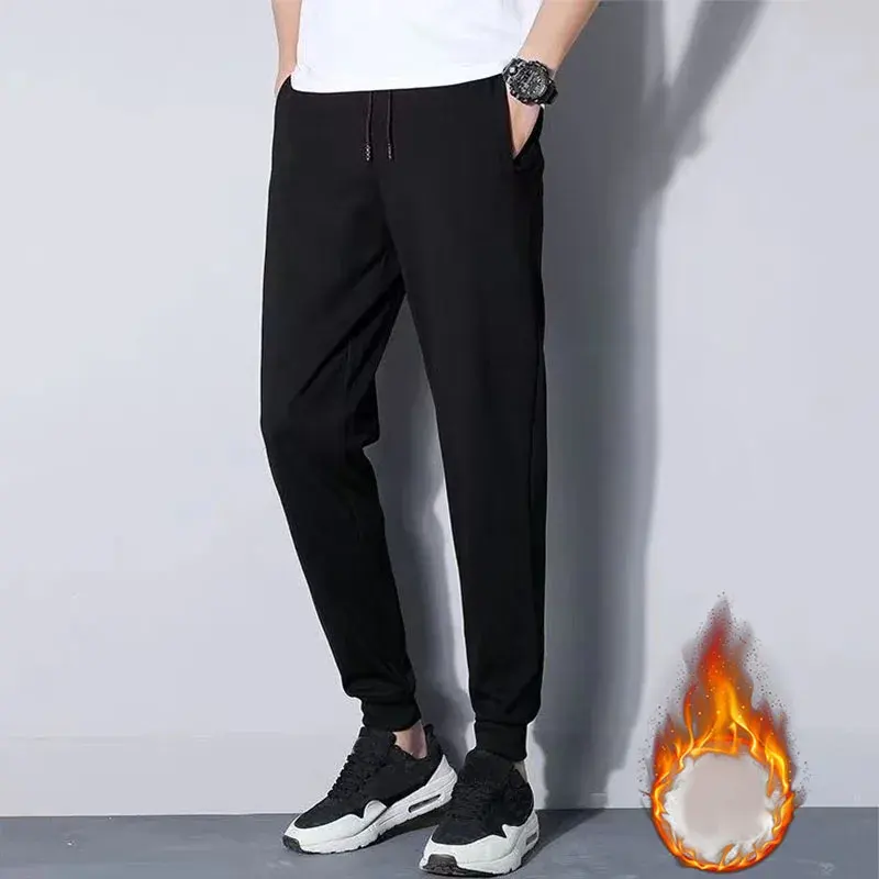 Černé pánské tepláky se zúženým střihem, vhodné pro volný čas, spolu s černobílými sportovními botami na neutrálním pozadí.