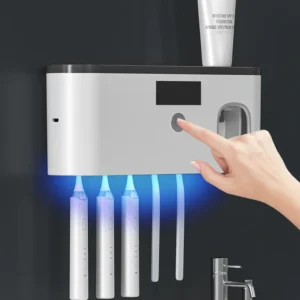 Elektrický držák na zubní kartáčky s UV sterilizací, na kterém je právě zapínán pomocí prstu a který je umístěn v koupelně vedle umyvadla.