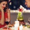 Romantická večera pri sviečkach s červeným vínom, muž drží sklenený kryt s ružou inšpirovanou rozprávkou Kráska a zviera, žena v červených šatách sa usmieva.