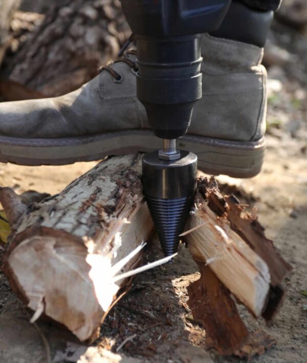 Dřevorubecká bota šlapající na hydraulický štípač dřeva, který rozštípává kládu na menší kusy pomocí šroubovitého mechanismu.