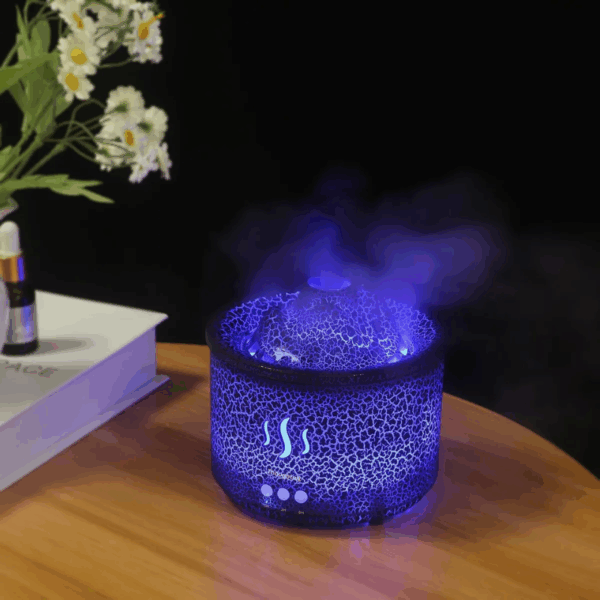 Modrý ultrazvukový aromadifuzér s praskajícím povrchem vyzařující fialové světlo, umístěný na dřevěném povrchu vedle bílých květin a knihy.