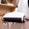 Bezdrátový zametač podlahy s bílým a černým designem zachycený při zametání drobků z lesklé podlahy, s elegantním ergonomickým tvarem a kolečky šetrnými k povrchu.