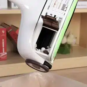 Bezdrátový zametač s bílým ergonomickým designem, který je zobrazen šikmo z profilu, s otevřeným úložným prostorem a černým kolečkem pro snadný pohyb.