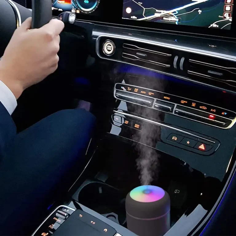 Interiér vozidla s navigáciou, rukou na volante a malým farebným difúzorom éterických olejov, ktorý vytvára jemnú vodnú paru v stredovej konzole.