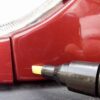 Detailní pohled na červenou karoserii automobilu s přiloženým opravným lakem pro opravu drobných škrábanců.