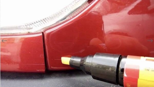 Detailní pohled na červenou karoserii automobilu s přiloženým opravným lakem pro opravu drobných škrábanců.
