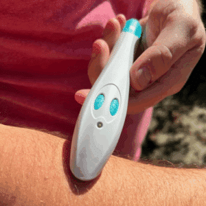 Bílý elektronický přístroj s tyrkysovými tlačítky se používá na předloktí, pravděpodobně se jedná o lékařské nebo kosmetické zařízení.