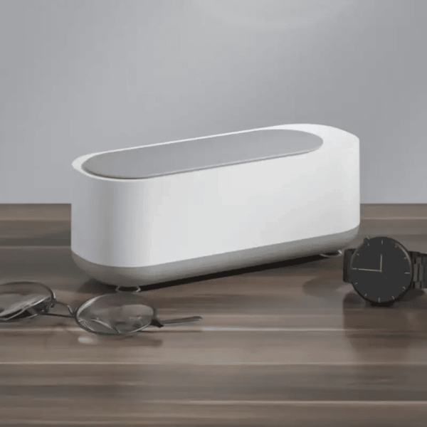 Bílý designový box nebo schránka na dřevěné podložce, vedle leží černé náramkové hodinky a brýle. Minimalistický a čistý design předmětu v neutrálních barvách.