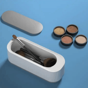 Bílý čisticí box na make-up štětce umístěný vedle čtyř barevných stínů na modrém pozadí, designový doplněk pro uchovávání a čištění kosmetických pomůcek.