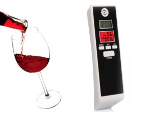 Digitální alkohol tester vedle sklenice červeného vína, který měří hladinu alkoholu v krvi.