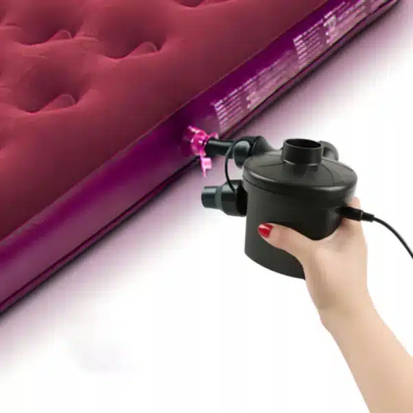 Elektrická pumpa v ruce nafukující červenou nafukovací matraci nebo postel, černá pumpa s připojeným elektrickým kabelem.