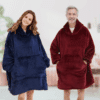 Žena a muž v modrém a červeném měkkém oversized mikrovláknovém oblečení, připomínajícím deku s kapucí, stojící vedle sebe s úsměvem.