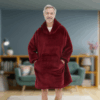 Starší muž v červené, měkké oversized mikině s kapucí stojí v obývacím pokoji s úsměvem na tváři a rukama v kapse.