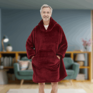 Starší muž v červené, měkké oversized mikině s kapucí stojí v obývacím pokoji s úsměvem na tváři a rukama v kapse.
