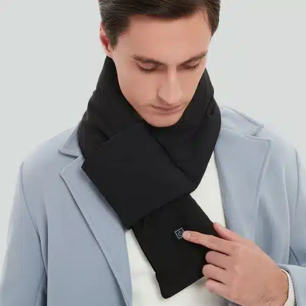 Muž v šedém kabátě s černou elektricky vyhřívanou šálou, která má připojené tlačítko pro ovládání teploty.