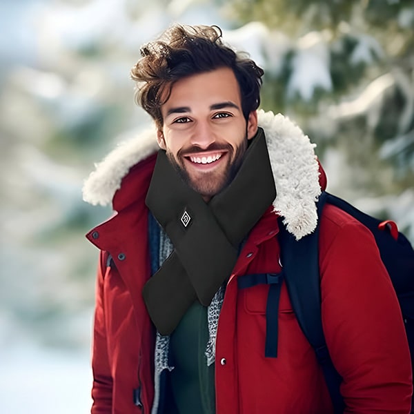 Muž v červené zimní bundě s kožíškem se usmívá do kamery, v pozadí zasněžené stromy a rozmazané zimní prostředí.