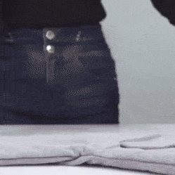 Černé džínové kalhoty s knoflíky, ležící na světlém povrchu v černobílém provedení.