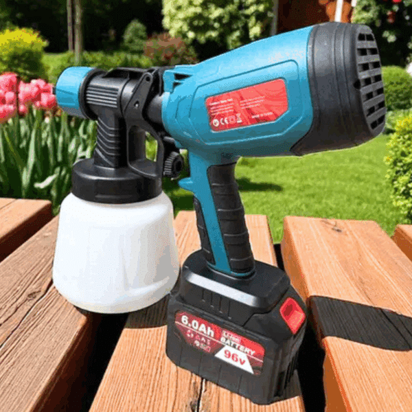 Modrá aku stříkací pistole s bílým nádobkou na barvu, položená na dřevěné terase se zahradou v pozadí, vybavená černou baterií s kapacitou 6,0 Ah.