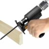 Ruční elektrická pila (ocaska) při řezání dřevěného materiálu, detail na černou rukověť a řezací nástroj v akci.