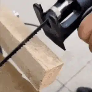 Ruční elektrická pila řezající dřevěný hranol na bílém pozadí, detail nástroje a řezné hrany.