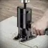 Černá elektrická ruční frézka nebo vyřezávací stroj, který je používán k opracování dřevěné desky s viditelnými pilinami.