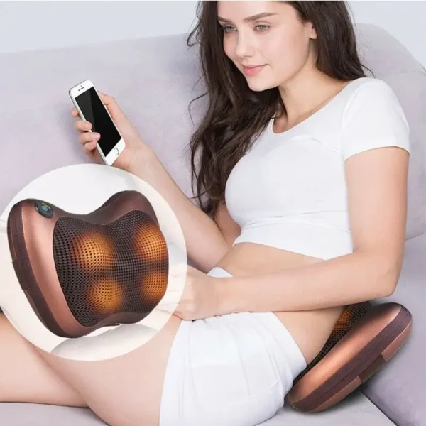 Žena sedící na gauči s mobilem v ruce a masážním polštářem, který používá k uvolnění svalů a relaxaci.