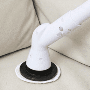 Bílá designová žehlička s černou podložkou, umístěná na světlém čalouněném povrchu, pravděpodobně na gauči nebo křesle.