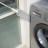 Pračka Siemens vedle okna, s hadrem na dlouhé tyči opřeným o bílou stěnu, v koupelně nebo prádelně.