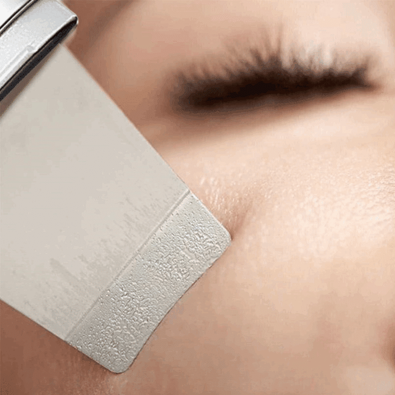 Detail mikroabrazivního nástroje těsně u lidské pokožky s rozmazaným pozadím řasy, který ukazuje postup kosmetického ošetření nebo úpravy povrchu pleti.