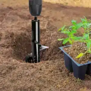 Zahradní vrták zapíchaný do hlíny vedle malé zelené rostliny v černém plastovém květináči, připravený na sázení.