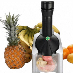 Přístroj na výrobu zmrzliny obklopený čerstvým ovocem - ananasem, banány a pomeranči, který právě vyrábí ovocnou zmrzlinu nebo sorbet.
